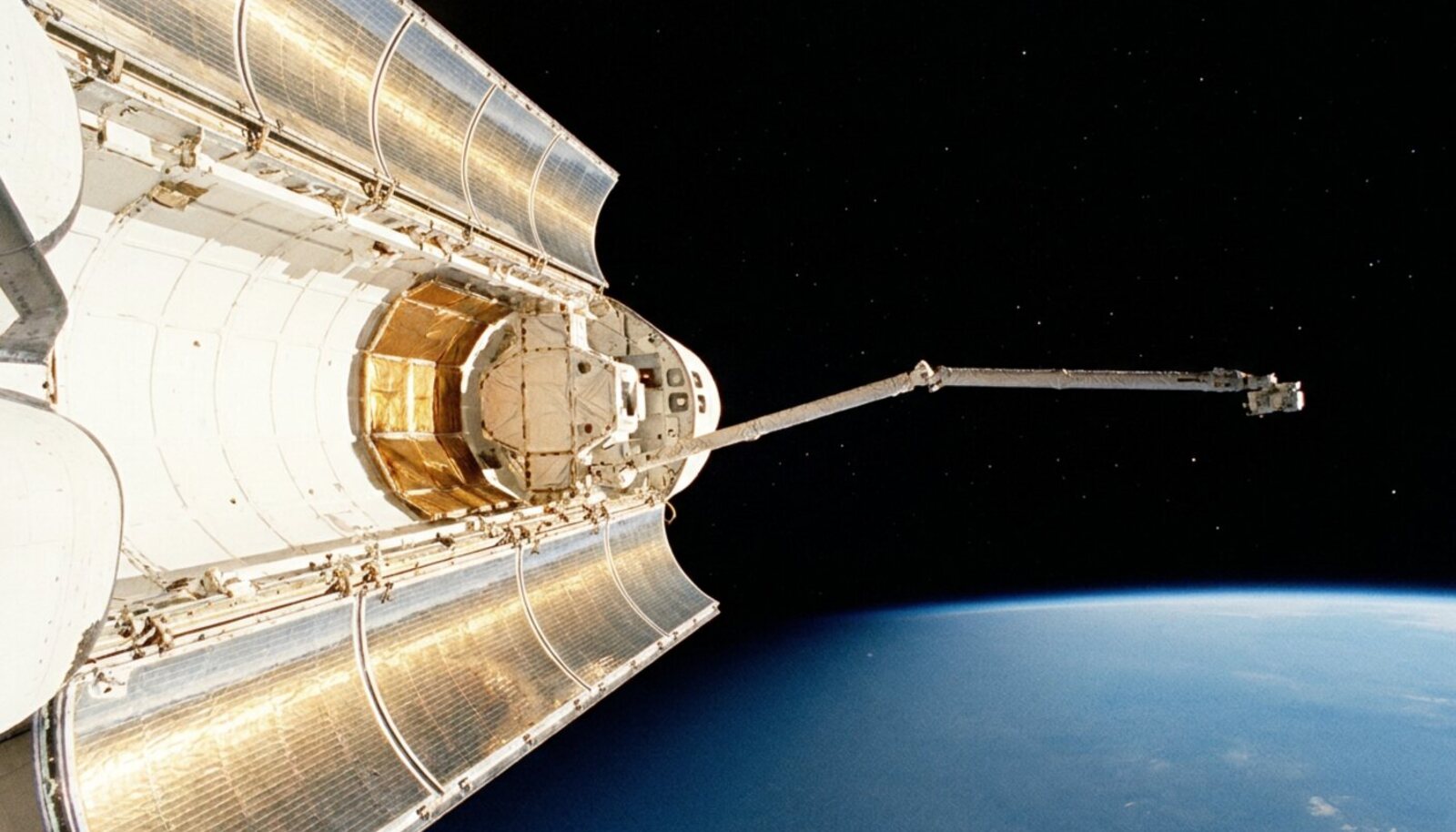 Space Shuttle payload bay with robot arm extended over Earth